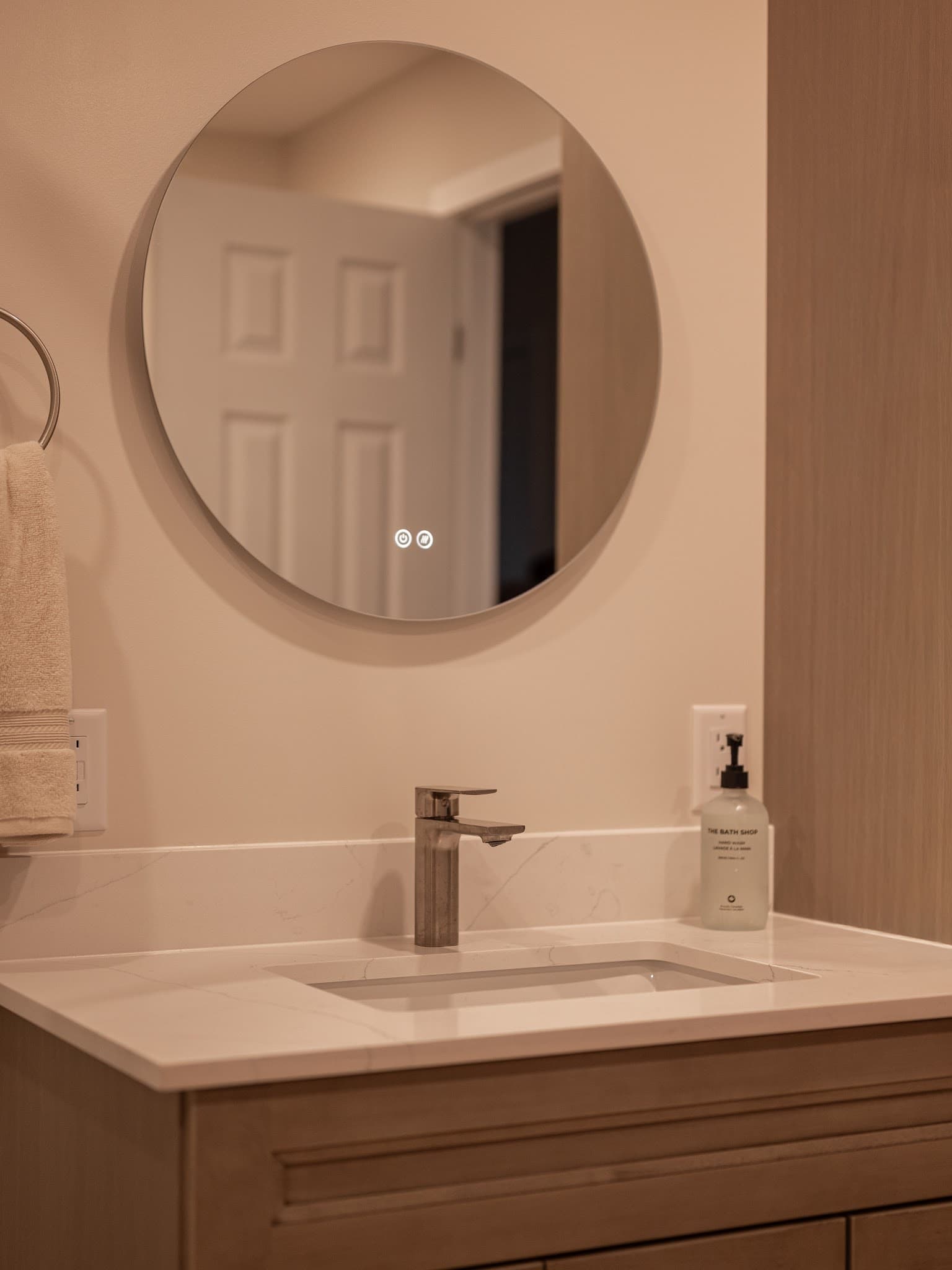 Vanity detail, round LED-touch mirror over quartz sink with brushed bronze faucet.