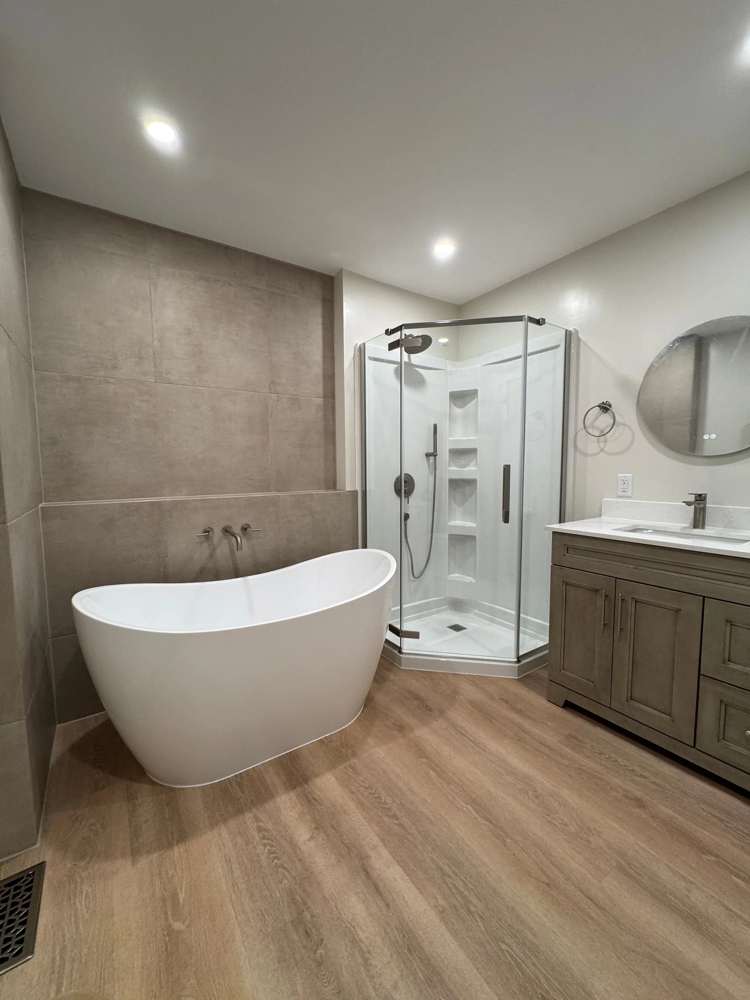 Renovated ensuite with freestanding soaker tub, walk-in glass shower, and double vanity on wood-look tile floor.