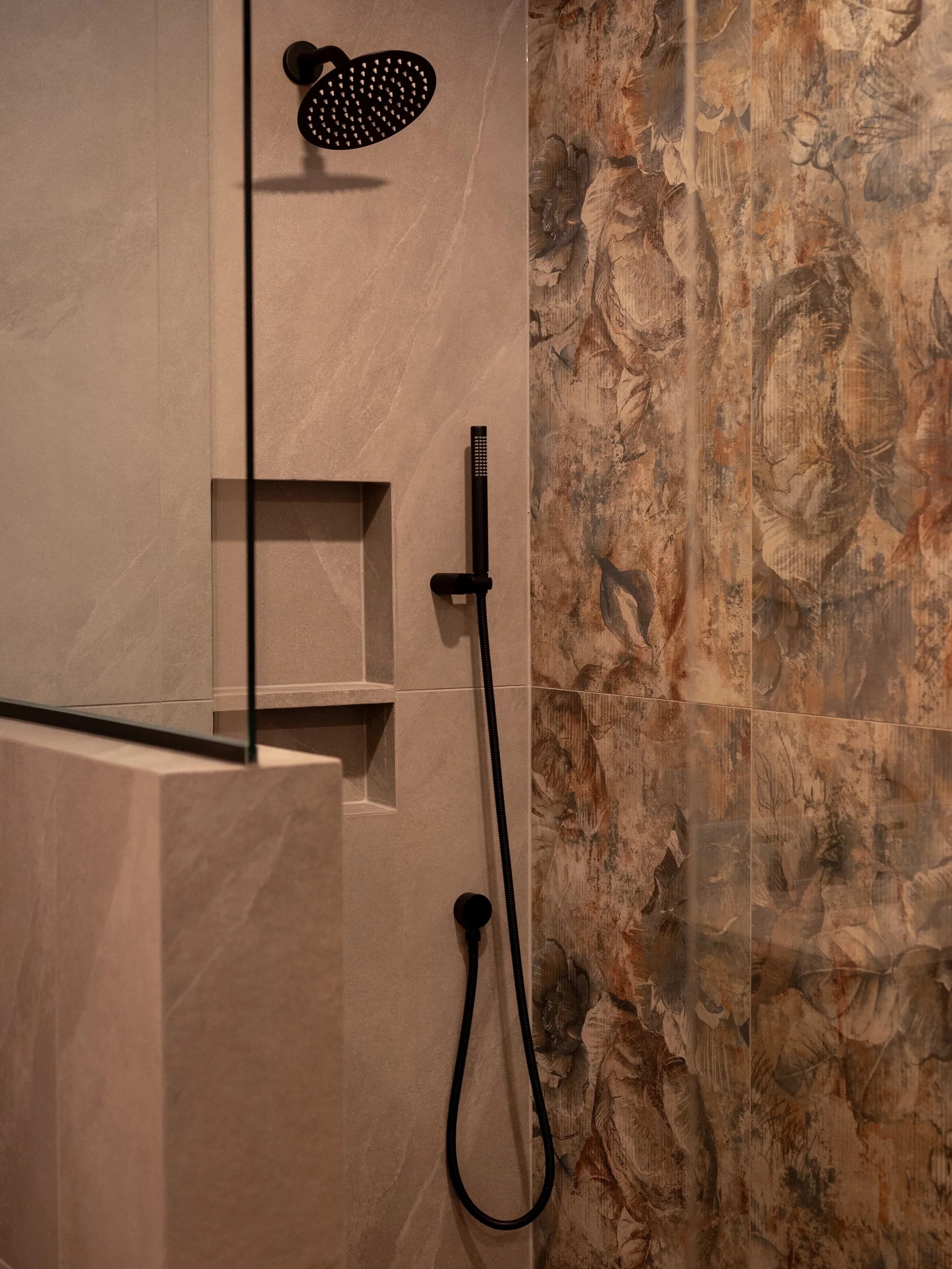 Walk-in tile shower with watercolor floral feature wall, matte black rainfall and handheld fixtures, built-in niche.