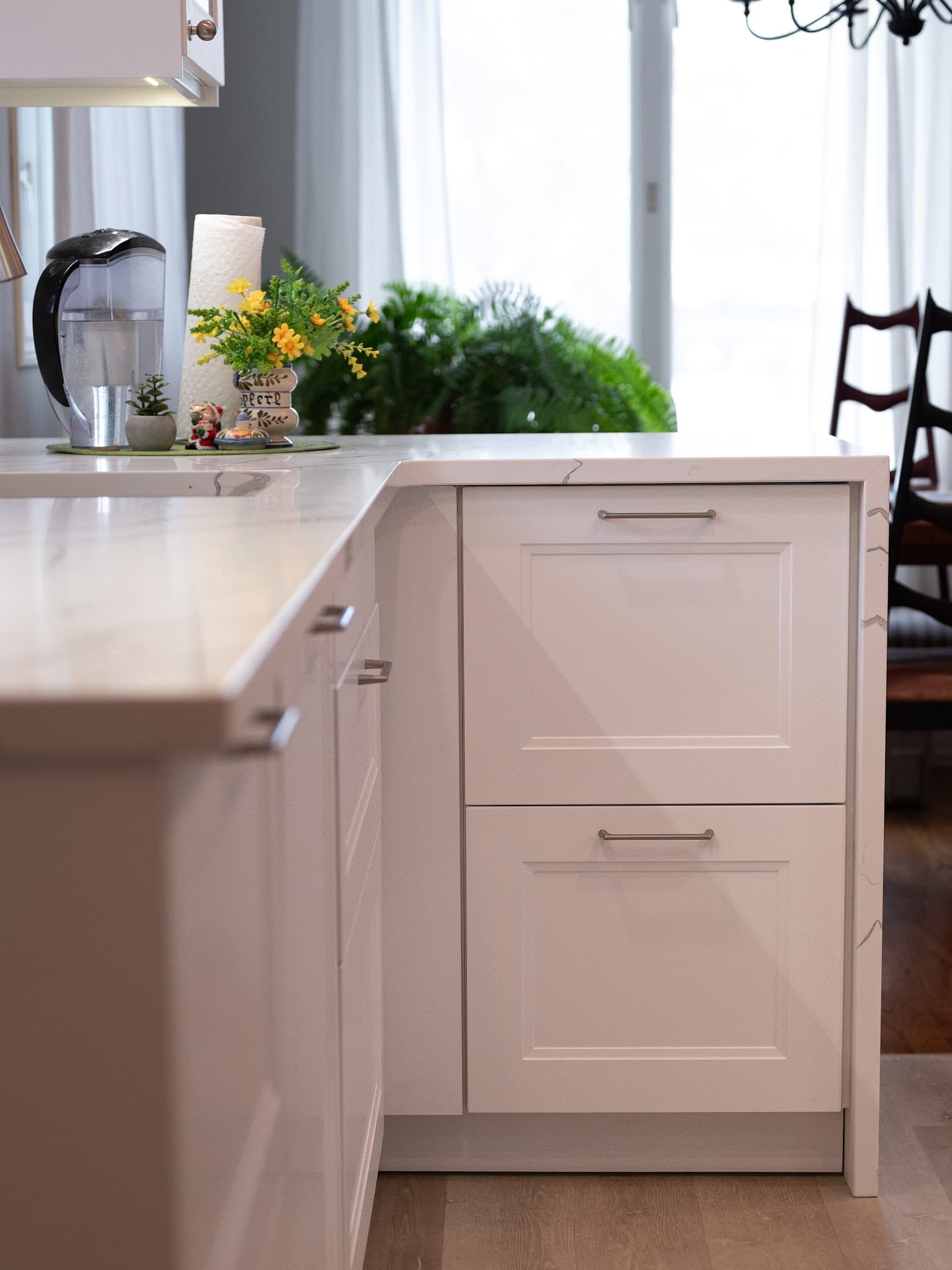 Renovated kitchen detail — white shaker cabinetry with marble-look quartz countertop and backsplash, soft window light.